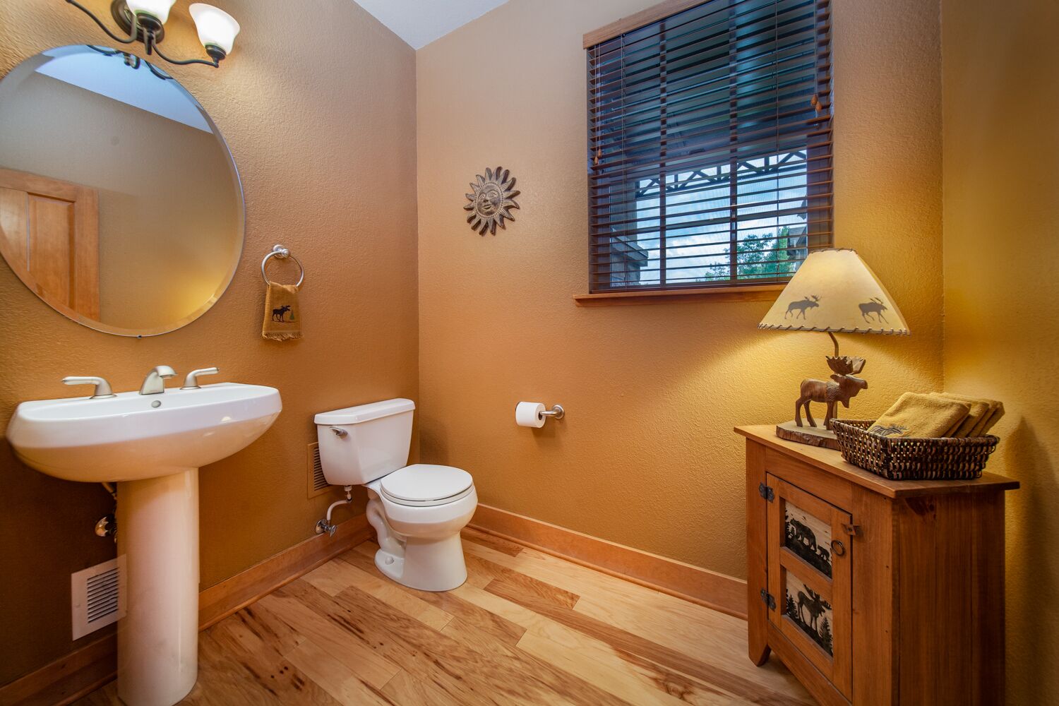 Une salle de bain avec un meuble-lavabo en bois, un miroir rond, un lavabo et des toilettes.