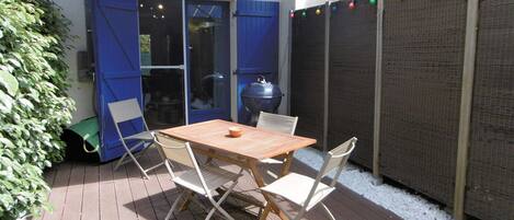 Un patio con mesa y sillas, una parrilla y una zona cubierta con contraventanas azules.