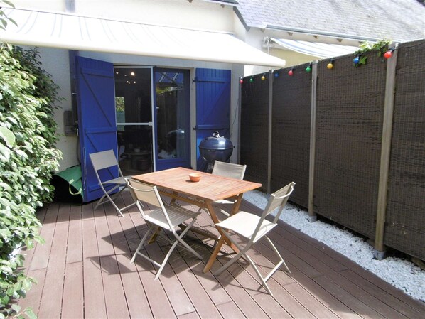 A patio with a table and chairs, a barbecue grill, and a covered area with blue shutters.