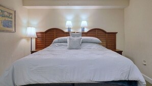 Un lit bien fait, avec une tête de lit en bois, deux lampes de chevet et un seul coussin décoratif.