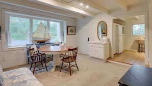 A cozy dining area with a wooden table and chairs, a sailboat decoration, and a kitchen with white cabinets and a wooden countertop. - 'Nantucket Cottage' w/ Fishing Dock + Sunsets (Fernandina Beach)