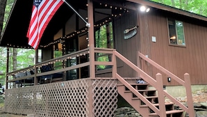 A cabin with a wooden exterior, a porch with a railing, a staircase, and an American flag. - Pocono Cabin in Masthope Mountain Community (Lackawaxen)