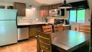 A kitchen with wooden cabinets, a stainless steel refrigerator, a microwave, and a stove. There is a dining table with chairs and a hanging light fixture. - Pocono Cabin in Masthope Mountain Community (Lackawaxen)