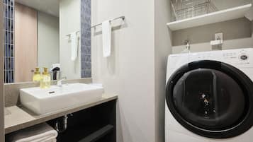 A modern bathroom with a sink, mirror, towel rack, and a front-loading washing machine.