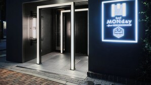 L’entrée d’un hôtel, ornée d’une enseigne au néon indiquant « MONday » et le statut « Premium ».