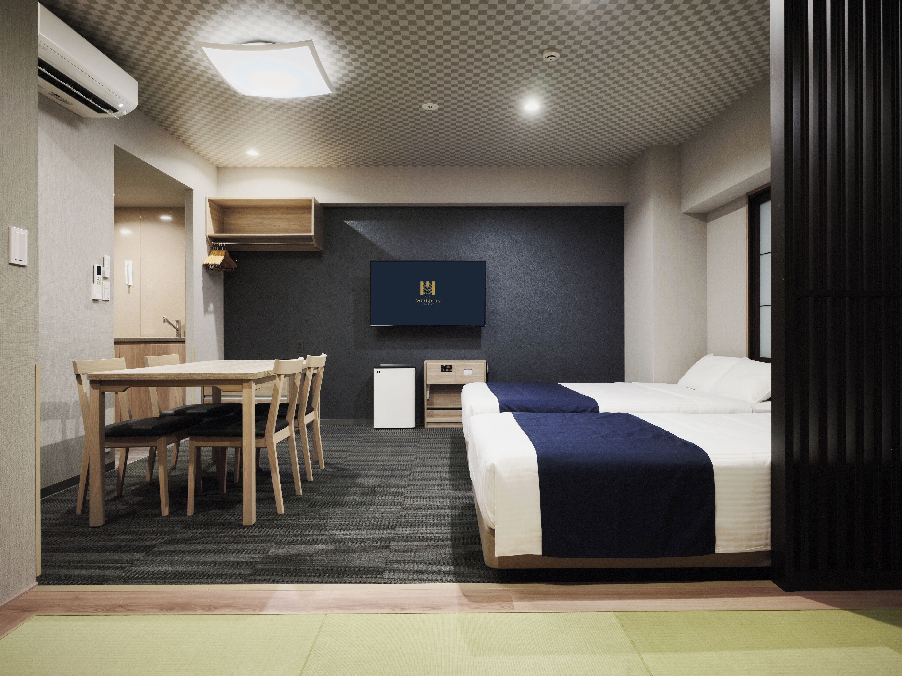 A hotel room with a bed, a desk, a chair, a TV, and a kitchenette.
