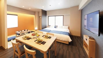 Una habitación de hotel con cama, televisión, una mesa de comedor con sillas y una kitchenette pequeña.