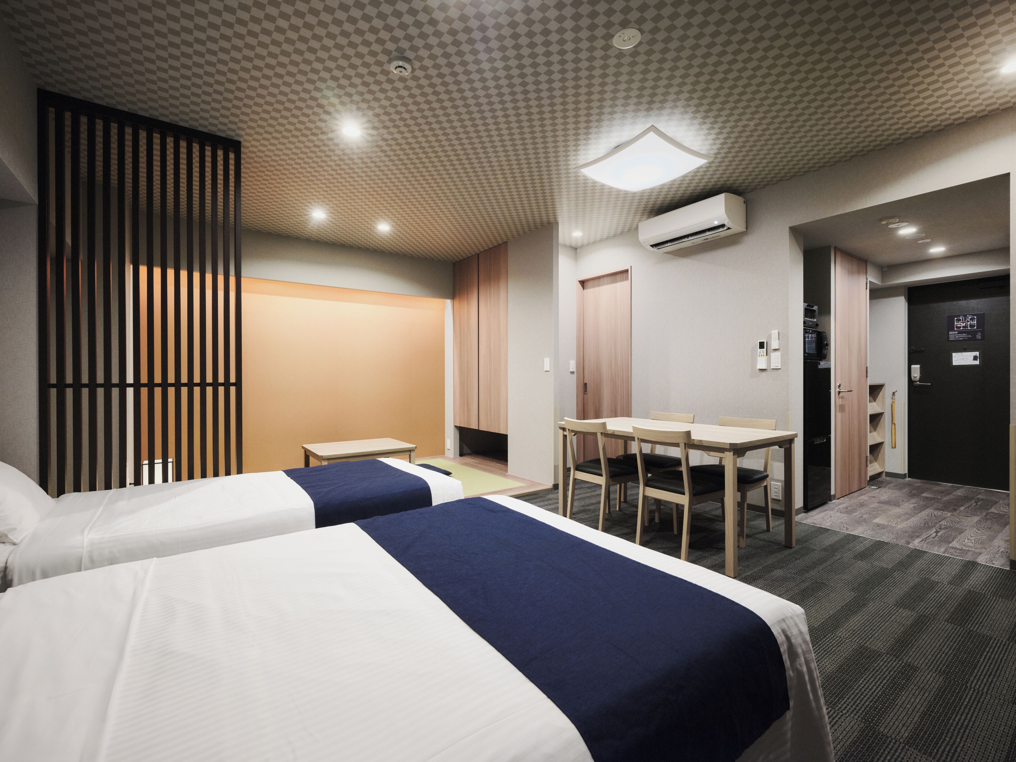 A hotel room with two beds, a desk, a chair, an air conditioning unit, and a door with a sign.