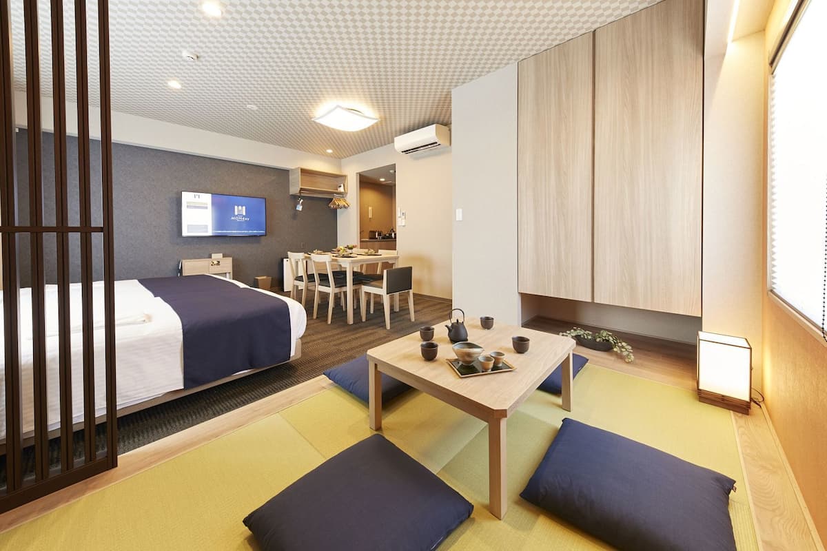 A hotel room with a bed, a desk with tea set, a TV, and a kitchenette.
