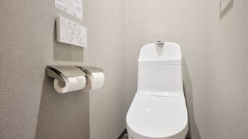 A modern bathroom with a toilet, a paper towel dispenser, and a hand dryer.