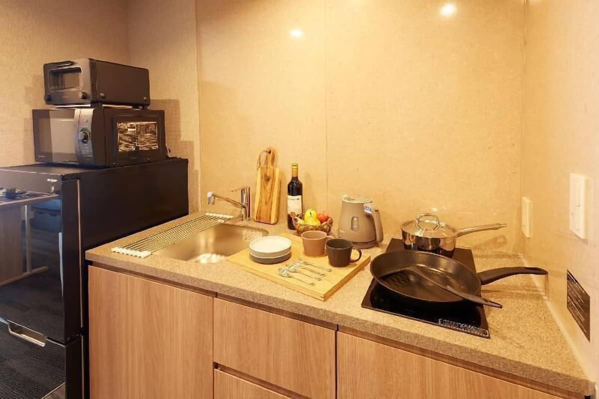 A compact kitchen with a sink, microwave, stove, and a small countertop area with a cutting board, utensils, and a bottle of wine.