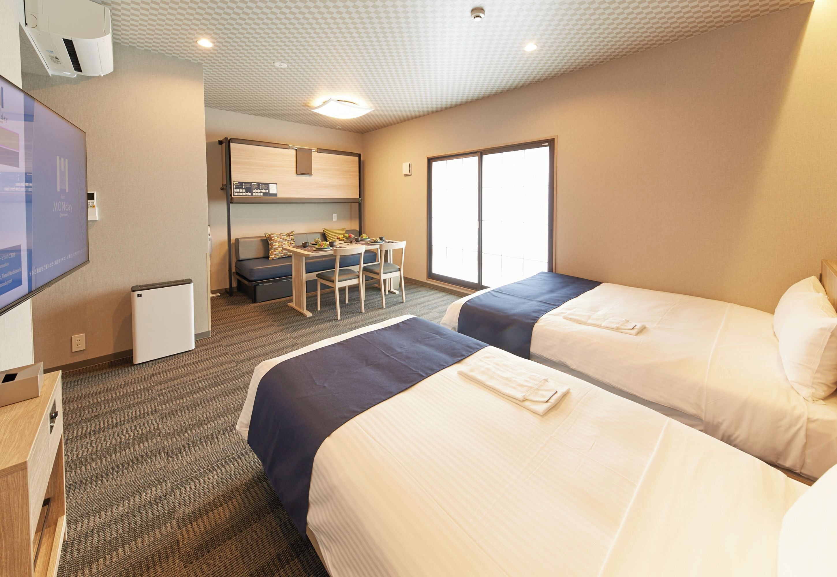 A hotel room with two beds, a desk, a chair, a television, and a small refrigerator.