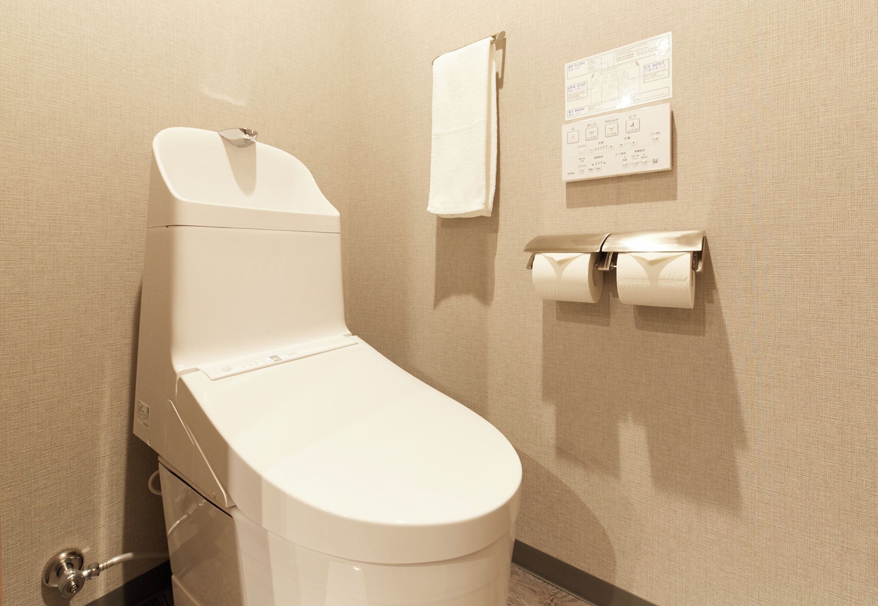 Eine moderne Toilette mit Wandpapierabroller und einem Handtuch an einem Haken.