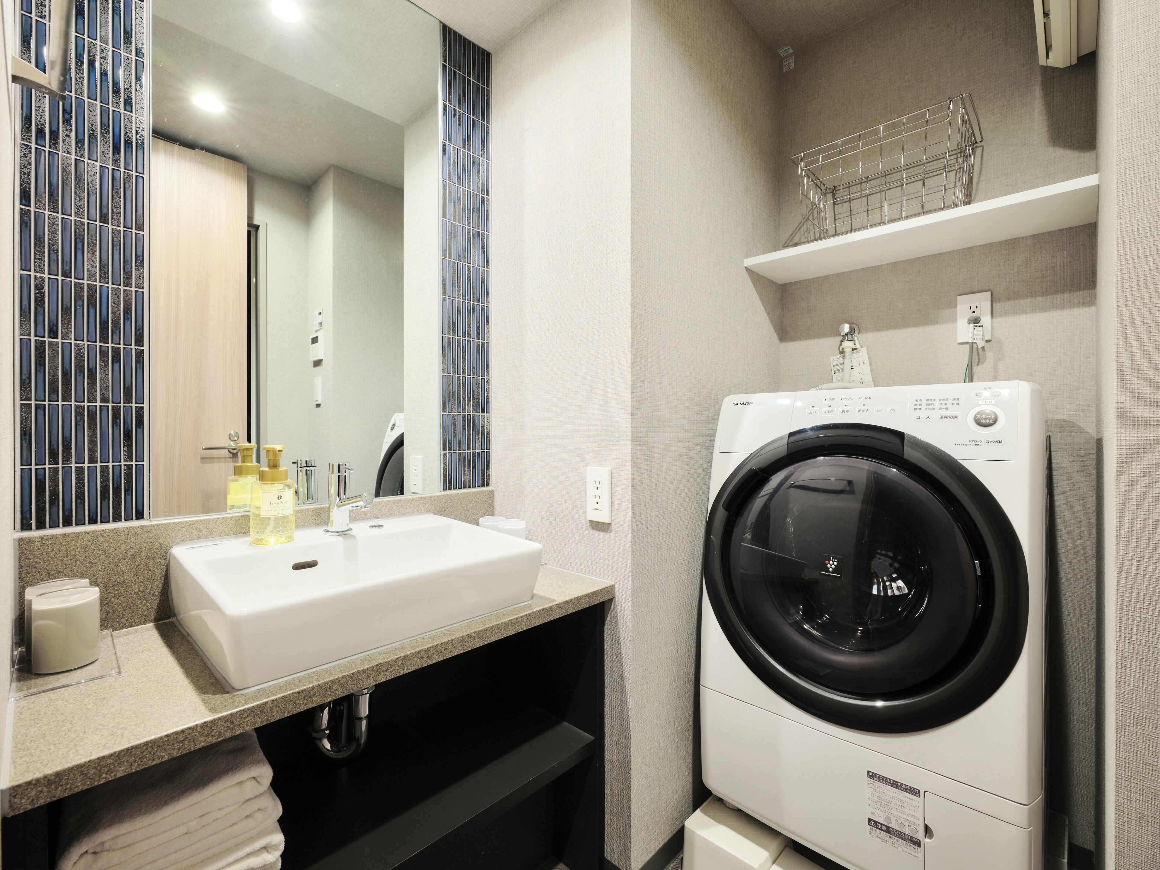 A modern bathroom with a sink, mirror, and a front-loading washing machine.