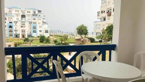Un balcon avec une table et des chaises blanches, donnant sur une cour intérieure où l’on aperçoit des bâtiments en arrière-plan.