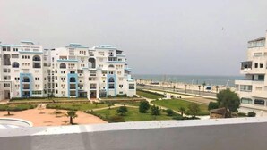 A residential building with multiple balconies, a courtyard with palm trees, and a view of the sea.
