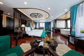 A modern hotel room with a curved ceiling, a large bed, a sitting area with a round table, and a view of the city through large windows. - La Regina Legend Cruise (Hai Phong)