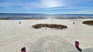 Una playa con una amplia zona arenosa, una estructura circular de piedra con diseño de brújula y un cielo despejado.