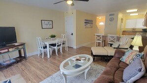 Sala de estar con televisor, mesa de comedor, sillas, sofá y área de cocina al fondo.
