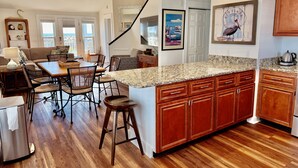 A modern kitchen with a granite countertop, wooden cabinets, and a dining area with wicker chairs and a table.