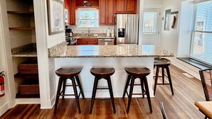A kitchen with a central island, wooden cabinets, a stainless steel refrigerator, and a window with blinds.