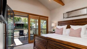 A bedroom with a large bed, a wooden headboard, a nightstand with a lamp, and a sliding glass door leading to an outdoor deck.