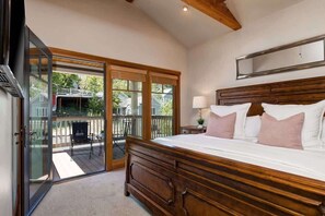 Quarto com uma cama grande, cabeceira de madeira, mesa de cabeceira com abajur e porta de vidro deslizante para um deck ao ar livre.