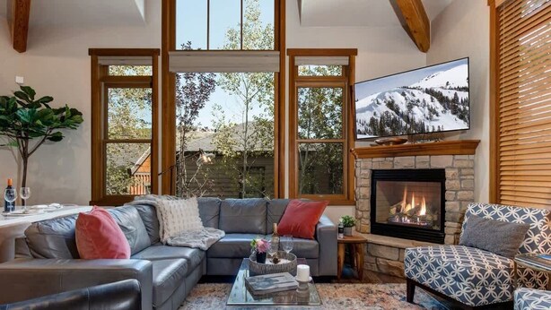 A living room with a fireplace, a television, and a large window overlooking a mountain.