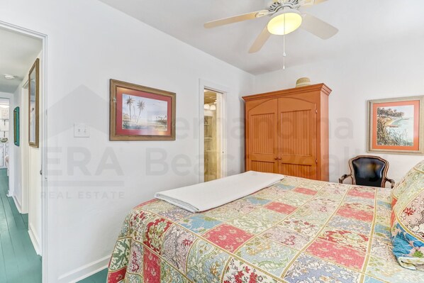 A bedroom with a bed, a wooden wardrobe, and two framed pictures on the wall.