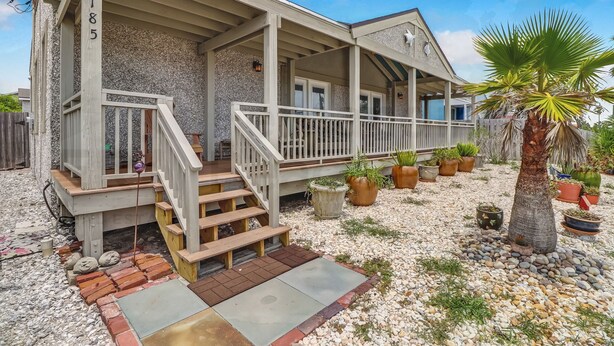 A house with a covered porch, a staircase, and a gravel driveway.