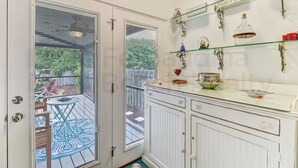 A room with a glass door leading to an outdoor patio, a white cabinet with glass shelves, and a decorative sign on the wall.