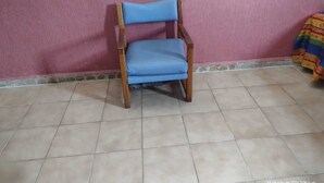 A chair with a blue cushion against a pink wall, on a tiled floor. - Hotel Verasol (Veracruz)