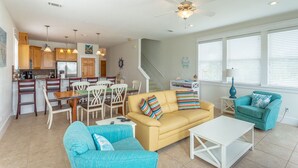 A spacious living area with a yellow sofa, teal armchairs, and a white coffee table. A kitchen with wooden cabinets and a dining area with a table and chairs is visible. - Fish, Beach, Pool, Swim, Relax in Luxury Rent for the month only 5,900.00 (Carrabelle)