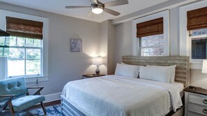 Ein Schlafzimmer mit einem Bett, einem Sessel, einem Nachttisch, einer Lampe und einem Deckenventilator.