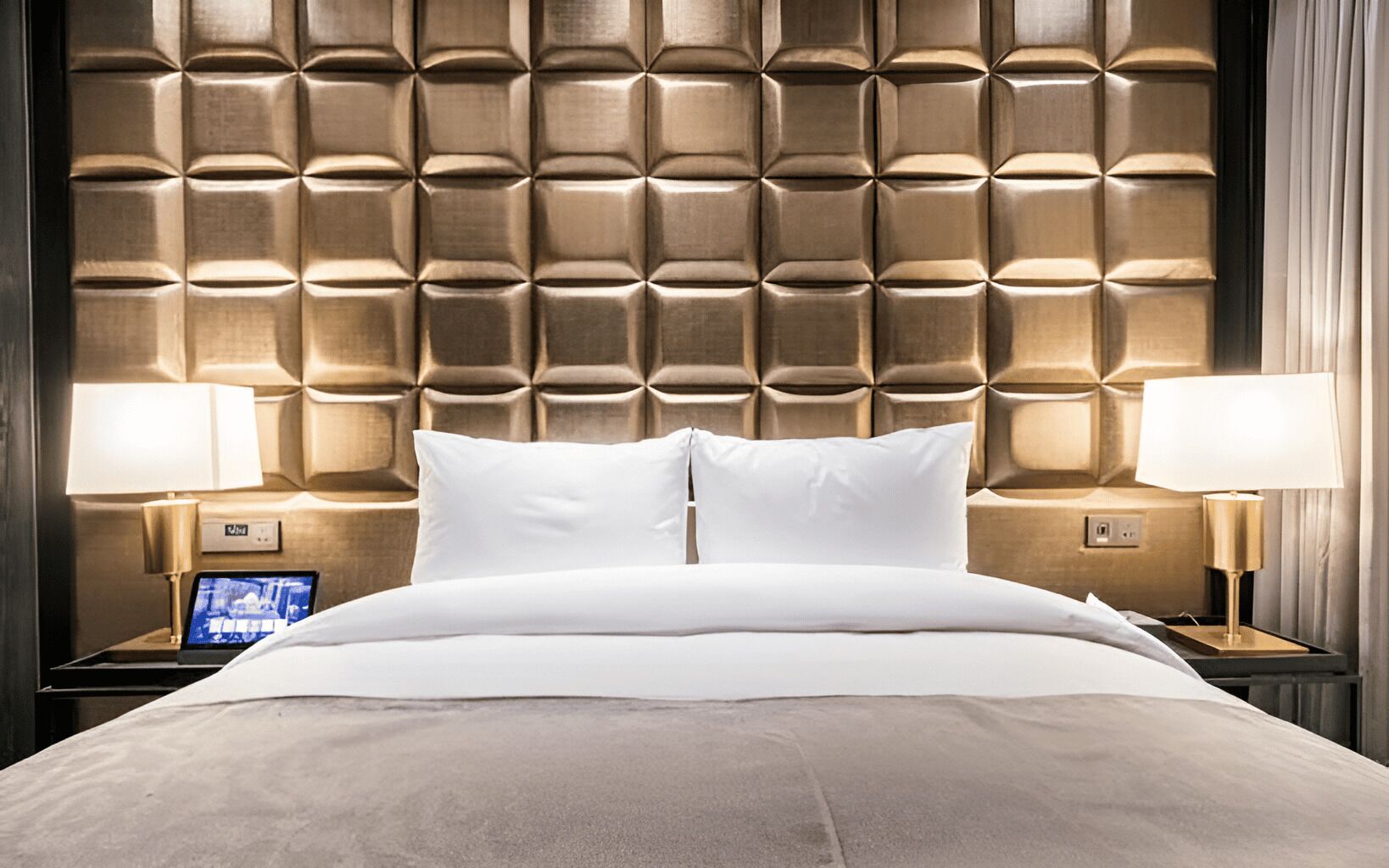 Habitación de hotel con tablero de cabecera capitonado, dos lámparas de noche, un televisor de pantalla plana y una cama con ropa blanca.