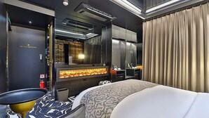 A modern hotel room with a large bed, a flat-screen TV, a fireplace, and a minibar. - Best Louis Hamilton Hotel Gijang (Busan)