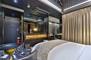 A modern hotel room with a large bed, a flat-screen TV, a fireplace, and a minibar. - Best Louis Hamilton Hotel Gijang (Busan)