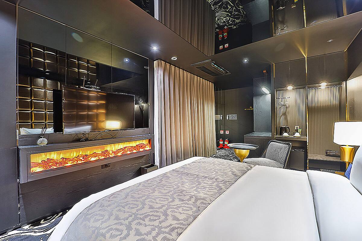 Una habitación de hotel moderna con una cama grande, televisión, chimenea, escritorio y espejo.