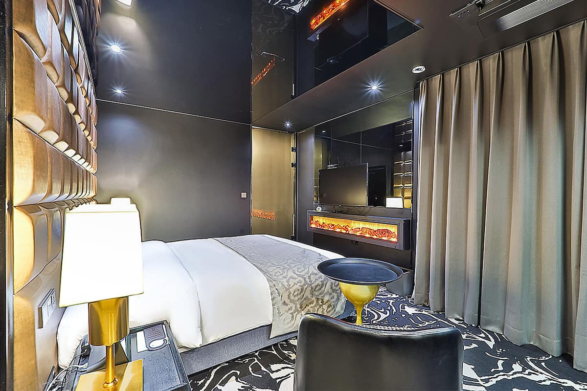 Una habitación de hotel moderna con una cama grande, un escritorio, una silla, una lámpara y un espejo.
