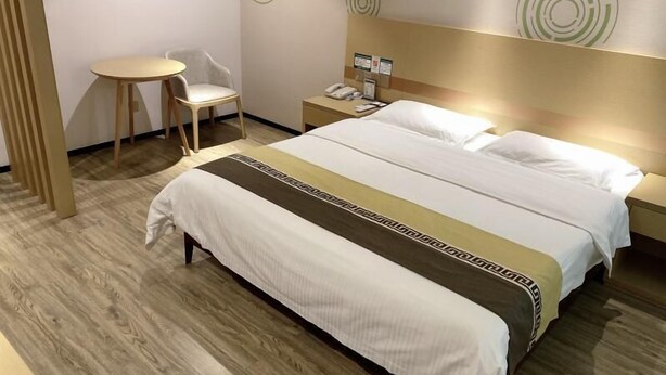 Hotellihuone, jossa on suuri sänky, yöpöytä, tuoli ja pieni pyöreä pöytä.