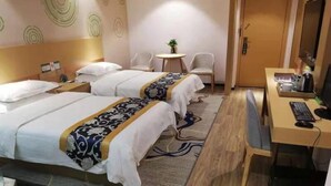 Hotellihuone, jossa on kaksi sänkyä, työpöytä tietokoneella, tuoli ja pieni pöytä, jonka päällä on kasvi.