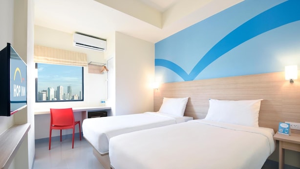 Habitación de hotel con dos camas, un escritorio, una silla roja, un televisor y vistas a la ciudad.