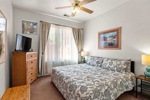 Un dormitorio con una cama, un televisor sobre un tocador, un ventilador de techo y un cuadro en la pared.