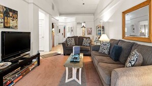 A living room with a flat-screen TV, a sofa, a coffee table, and a bookshelf. - Light, Bright, Stylish Condo Nepenthe West Sedona (Sedona)