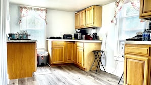 Cocina compacta con armarios de madera, una encimera con electrodomésticos y un taburete pequeño.