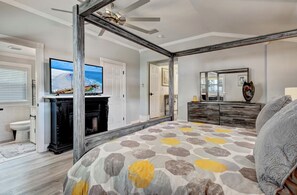 Een slaapkamer met een bed, een televisie, een open haard, een dressoir en een spiegel.