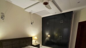 A bedroom with a bed, a wardrobe, a ceiling fan, and a nightstand with a lamp.