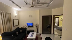 A living room with a black sofa, a white coffee table, a television, and a ceiling fan.