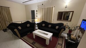 A living room with two black sofas, a white coffee table, a patterned rug, a TV, and a vase with flowers.