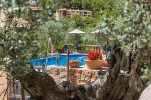 A pool area with a stone wall, potted plants, and umbrellas. - Stunning Mountain Views and Pool – Villas Ca'n Tamany & Ca'n Baixo (soller)